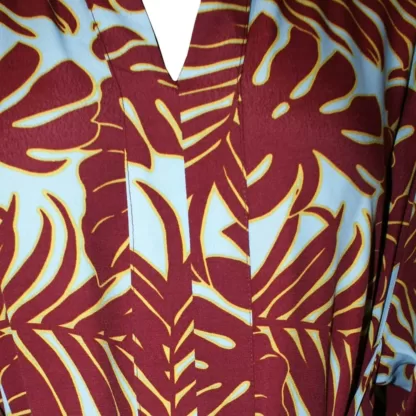 The Everywhere Dress in Maroon Leaves is a maxi dress with a built in tie belt that pulls the dress together with a tie in front. The front neck is bordered with same fabric facing and the long skirt has a centred small slit at the bottom. It as long sleeves. Front neckline close up view