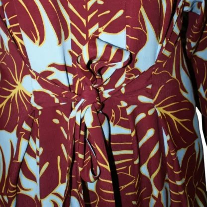 The Everywhere Dress in Maroon Leaves is a maxi dress with a built in tie belt that pulls the dress together with a tie in front. The front neck is bordered with same fabric facing and the long skirt has a centred small slit at the bottom. It as long sleeves. Front tie view